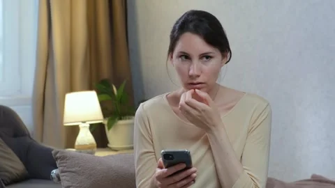 Woman looks at the smartphone screen while sitting on the couch and gets scared Stock Footage 242597809