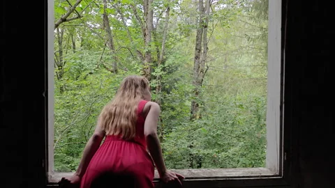 Woman looks through an open window frame toward a forest Stock Footage 346076271