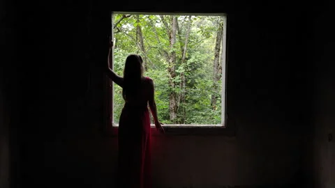Woman looks through an open window frame toward a forest Stock Footage 346076546