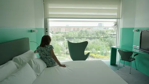 Woman lowering the automatic blinds of a large window overlooking the city. Stockbeeldmateriaal 242116302