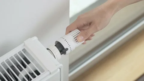 The woman lowers the radiator temperature to the minimum economical heating mode 库存影片 211621237