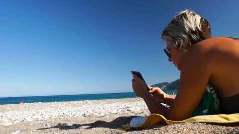 Woman lying on beach and using phone on summer travel vacation. Video stock 108331316