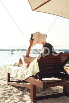 Woman Lying On A Beach Chair Reading A Book