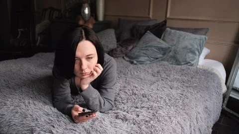 Woman lying on the bed and checking her smartphone looking satisfied Stock Footage 104560705