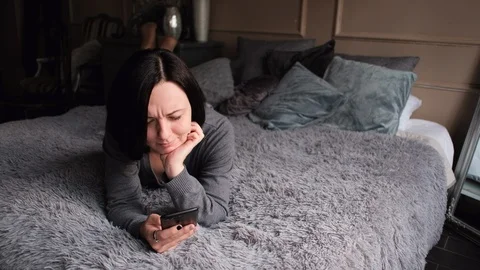 Woman lying on the bed and checking her smartphone looking dissapionted Stock Footage 104561121