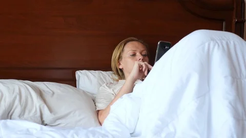 The woman is lying in bed and using a smartphone. 4k, slow motion Stock Footage