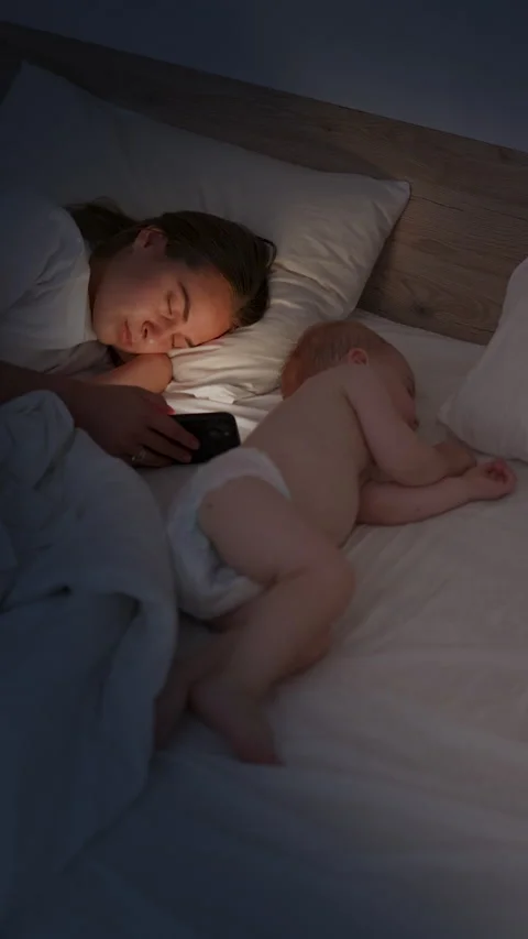 Woman lying in bed with baby, using smartphone while child sleeps peacefully Stock Footage 341897286