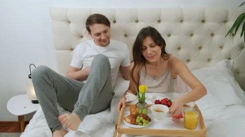 Woman is lying in bed with the breakfast while her husband come and kiss her. Stock Footage 147132634