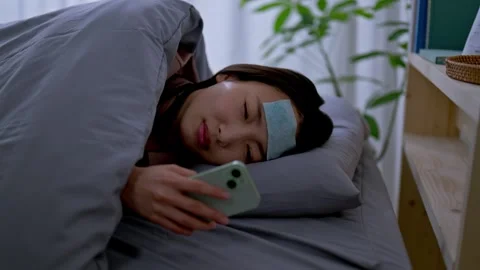Woman lying in bed with a cooling sheet and using her smartphone Stock Footage 336766973