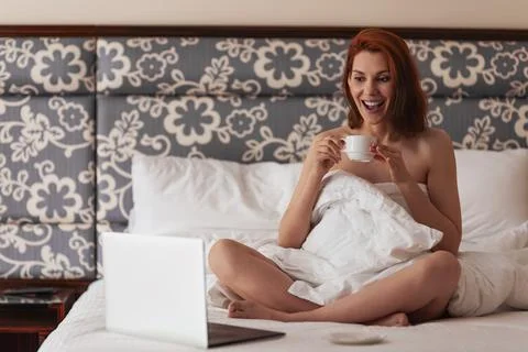 Woman lying in bed with laptop drinking coffee and working. Beautiful blonde 写真素材