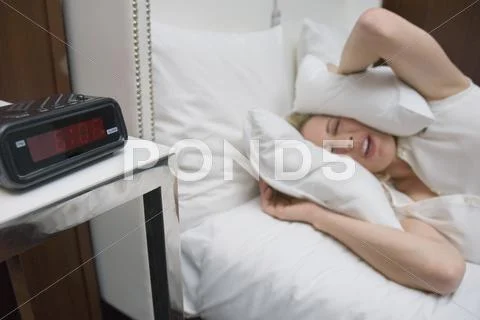 Woman lying in bed with pillows covering her ears ignoring alarm clock Stock Photos