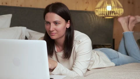 Woman lying on bed using laptop in cozy bedroom Stock Footage 303497063