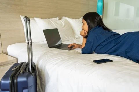 Woman lying on bed while using laptop during business trip Foto stock