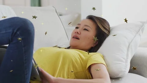 Woman lying on couch moving tablet, tapping while using tech app, gold stars Stock Footage 333873699