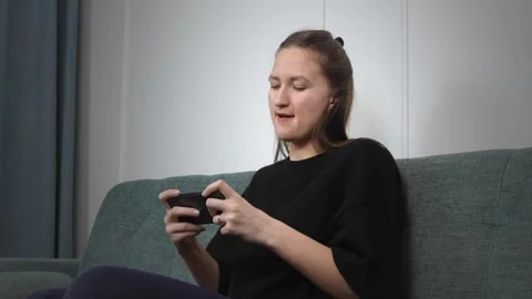 Woman lying on couch playing mobile game with enthusiasm 库存影片 308236333