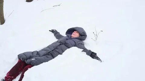 Woman lying in deep snow making a snow angel and laughing Video stock 329107861