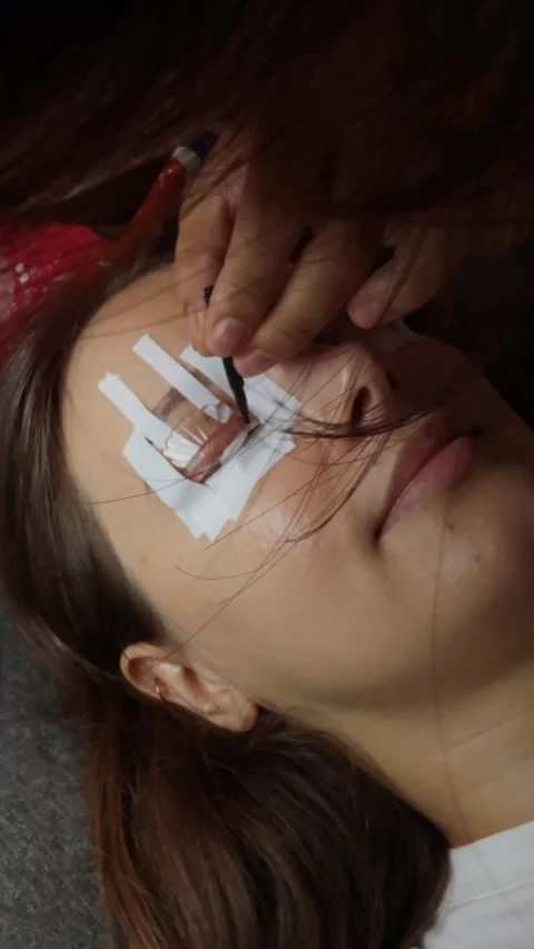 Woman lying down with eye pads and tape during an eyelash extension procedure, a Stock Footage 332816580