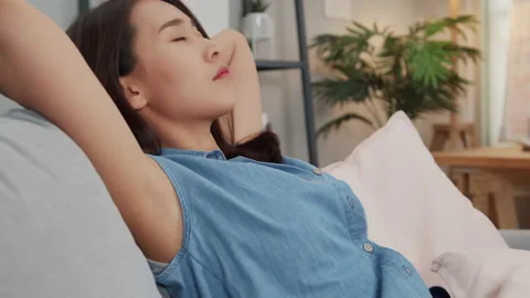 Woman Lying down on sofa close her eye breathing fresh air relaxing at home Stock Footage 132811397