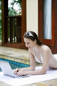 Woman lying forward by the poolside using laptop Stock Photos