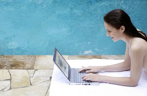 Woman lying forward by the poolside using laptop Foto stock