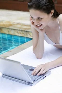 Woman lying forward by the poolside using laptop Stock Photos