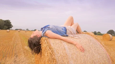 Woman lying on her back on haystack with arms outstretched Stock Footage 100901234