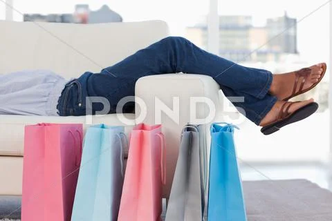 Woman lying on her sofa with shopping bags on the floor Stock Photos