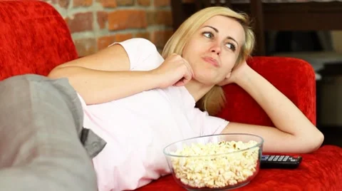 Woman lying on sofa, eating popcorn and watching tv HD Stock Footage