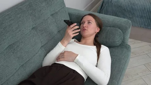 Woman lying on sofa using smartphone, sending voice message Stock Footage 308228756