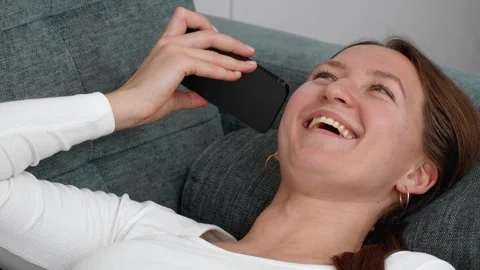 Woman lying on sofa using smartphone, changing facial expressions Stock Footage 308228768