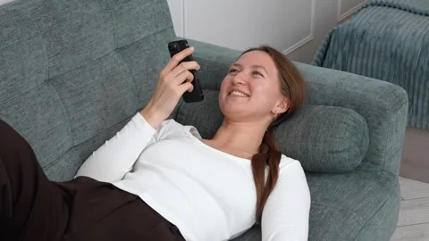 Woman lying on sofa using smartphone, sending voice message Video stock 308228938