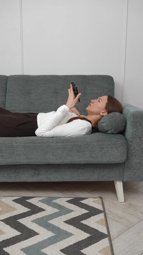 Woman lying on sofa using smartphone, sending voice message Stock Footage 308234678