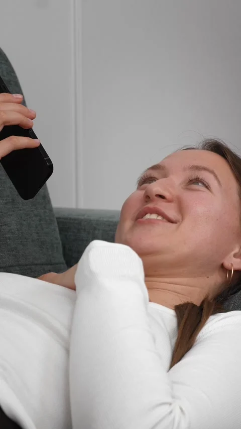 Woman lying on sofa using smartphone, changing facial expressions Stock Footage 308234722
