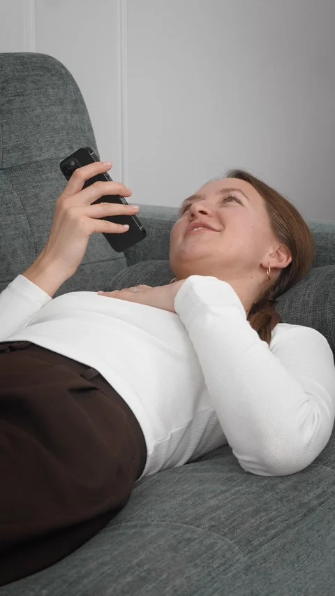 Woman lying on sofa using smartphone, sending voice message Stock Footage 308235702
