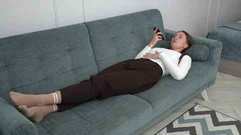 Woman lying on sofa using smartphone, sending voice message Vidéo 308235738