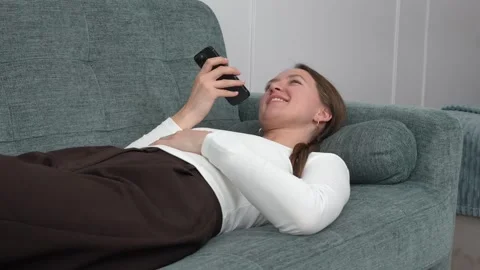 Woman lying on sofa using smartphone, sending voice message Vídeos de archivo 308258343