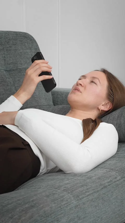 Woman lying on sofa using smartphone, sending voice message Stock Footage 308259016