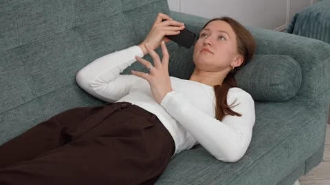 Woman lying on sofa using smartphone, recording voice message Stock Footage 308318164
