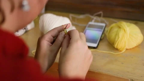 A woman Makes a complicated loop, she knits a yellow baby bootie. On the table: Stock Footage 144110070