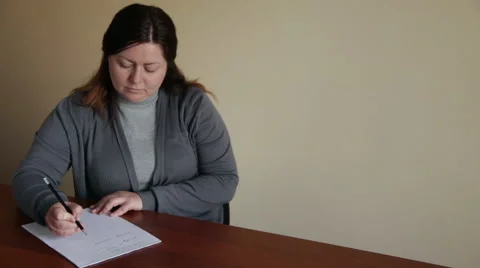 A woman makes an entry on a sheet of paper at the table Stock Footage 48484811