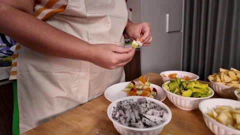 A woman makes fruit kebabs, stringing pieces of fruit on a skewer, stands at a Stock Footage 329939437