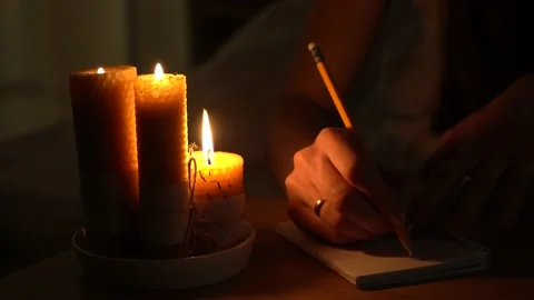 A woman makes notes in a notebook in a dark room with burning candles. Vídeos de archivo 235786612