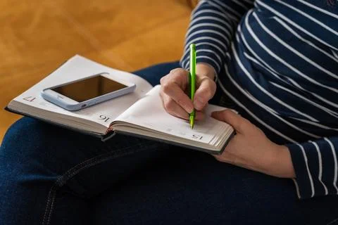 Woman makes notes in a notebook while working with a smartphone Stock Photos
