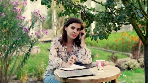 Woman making notes during cellphone call in the garden Stock Footage 128607322
