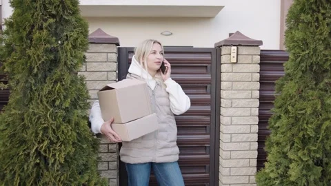 Woman making a phone call while delivering packages to a house entrance Stock Footage 305253707
