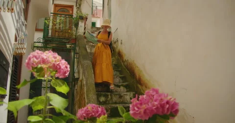 Woman with map in hands walking down stone steps in floral alley of Amalfi town Stock Footage 308261902