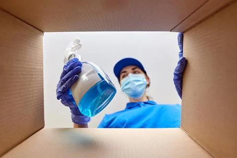 Woman in mask packing cleaning supplies in box Stock Photos