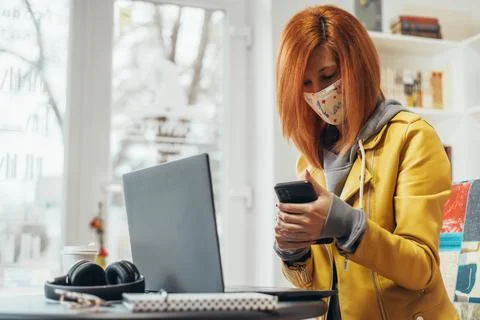Woman with mask using smartphone and laptop in the office Stock Photos