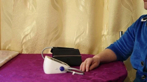 A woman measures pressure using an automatic blood pressure monitor. Sitting on  Stock Footage 73447114