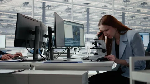 Woman in microelectronic facility studies microchip architecture with microscope Stock Footage 335879318